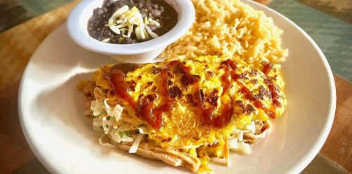 A plate featuring a cheesy omelet over shredded chicken, served with rice and black beans topped with cheese.