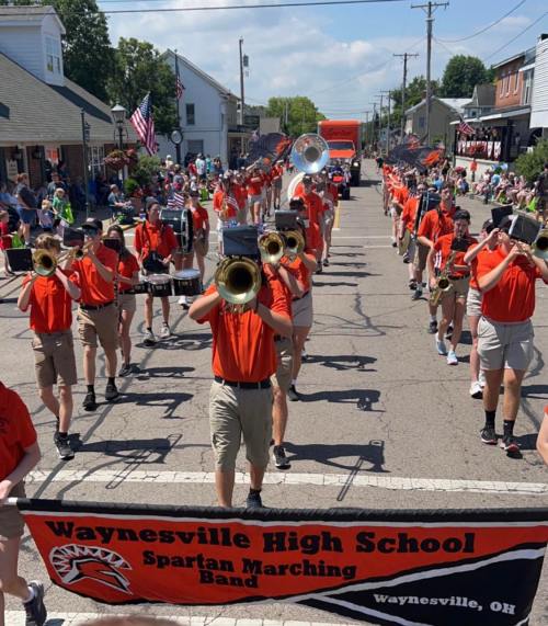 Waynesville High School Spartan Marching Band performing in a parade, wearing orange shirts and playing instruments.