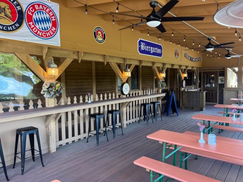 A cozy outdoor seating area with wooden tables, stools, and decorative signs, resembling a traditional beer garden.
