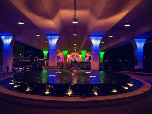 A vibrant, illuminated space with colorful pillars and a circular water feature reflecting lights at night.