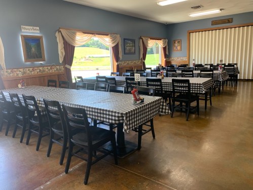 A spacious dining room with checkered tablecloths, black chairs, and large windows overlooking a green landscape.