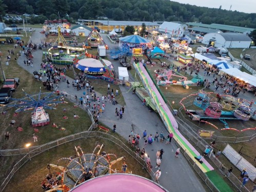 Aerial view of a lively fairground with rides, games, and crowds enjoying the festivities at dusk.