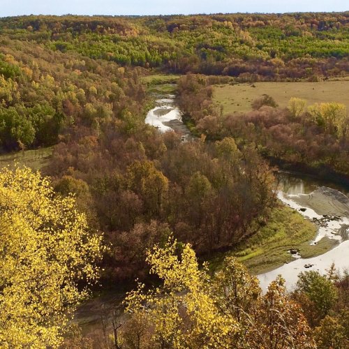 A scenic view of a winding river surrounded by vibrant autumn foliage and rolling hills.