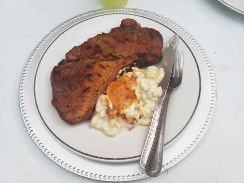A grilled steak served on a plate with creamy macaroni and cheese, accompanied by a knife and fork.