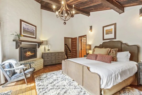 Cozy bedroom with a fireplace, wooden beams, a large bed, and decorative artwork on the walls.