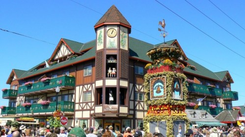 A large, decorative building with a clock tower, surrounded by crowds and colorful flower displays on a sunny day.
