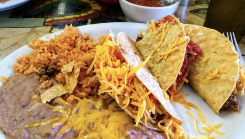 A plate of tacos topped with cheese and salsa, served with rice and refried beans on the side.