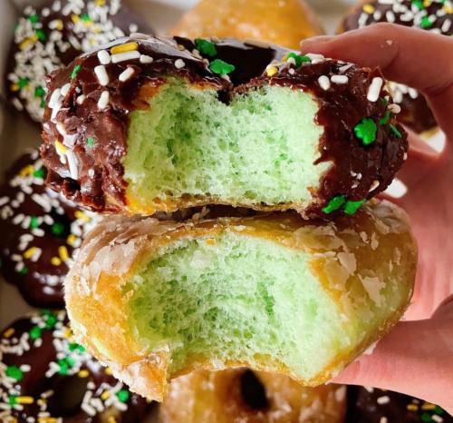 A hand holds two donuts: one chocolate-covered with sprinkles and one glazed, both with a green interior.