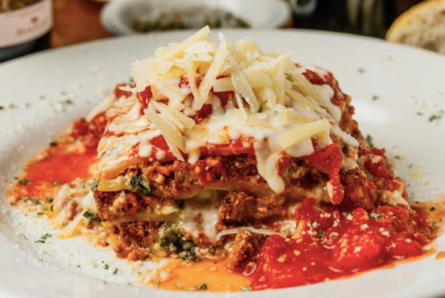 A delicious serving of lasagna topped with marinara sauce and shredded cheese, garnished with herbs on a white plate.