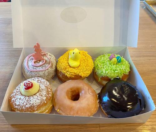 A box of six colorful donuts, featuring various toppings like sprinkles, frosting, and decorative candies.