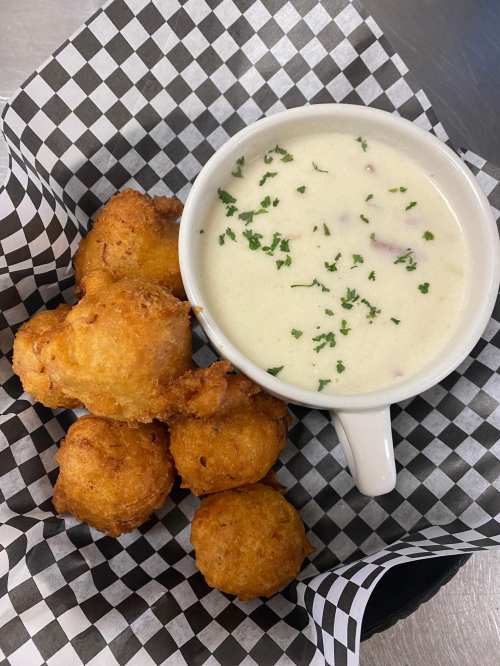 A basket with golden fried balls and a small cup of creamy soup garnished with parsley, all in a checkered paper liner.