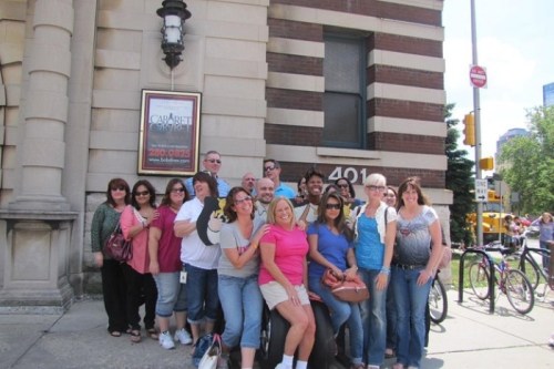 A group of people posing together outside a building on a sunny day, with bicycles parked nearby.