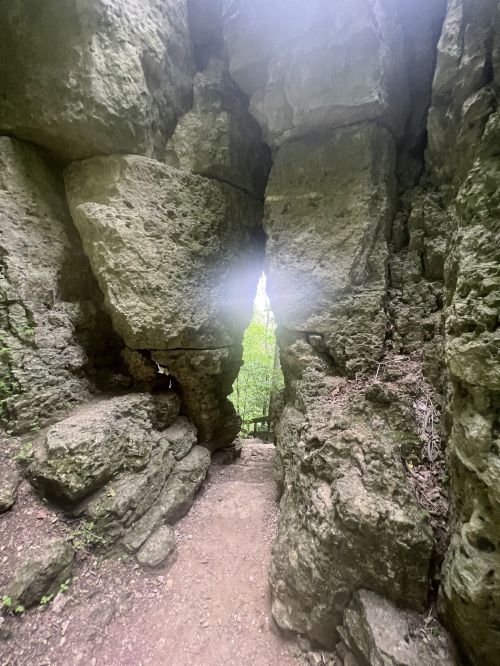 A narrow passageway between large, rugged stone formations in a lush, green forest.