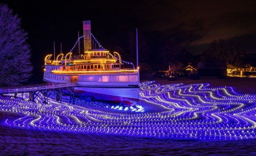 A brightly lit boat on a dock, surrounded by glowing blue lights resembling waves under a night sky.