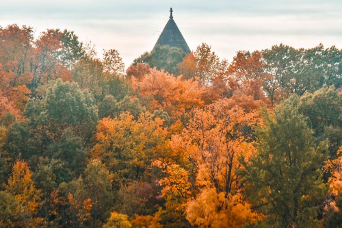 A vibrant autumn landscape with colorful trees and a church steeple peeking through the foliage.