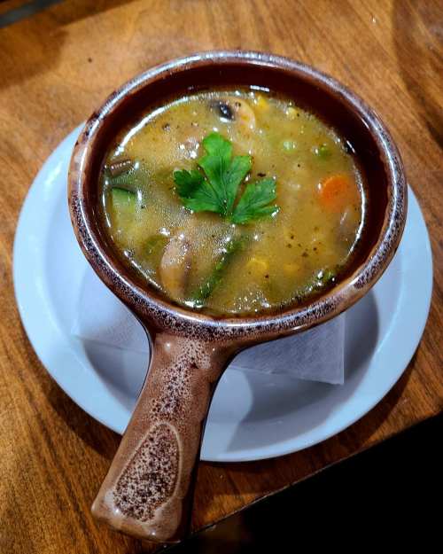 A bowl of hearty vegetable soup garnished with a sprig of parsley, resting on a wooden table.