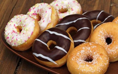 A plate of assorted donuts, including chocolate, glazed, and frosted with sprinkles, on a wooden table.