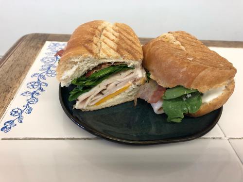 A sandwich with turkey, cheese, spinach, and tomato, cut in half and served on a dark plate.