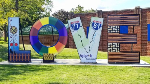 Colorful "LOVE" sign featuring designs representing local attractions and highways, set in a grassy area.