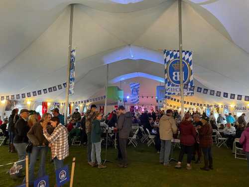 A large tent filled with people socializing, decorated with banners and lights, during a festive event.