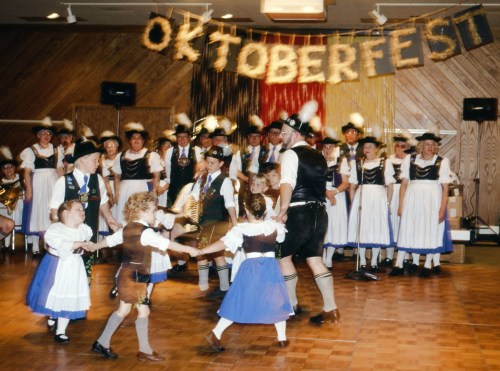 A lively Oktoberfest celebration with people in traditional attire dancing and a festive banner in the background.