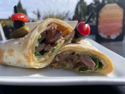 A close-up of a beef wrap filled with greens, served on a plate, garnished with cherry tomatoes and olives.