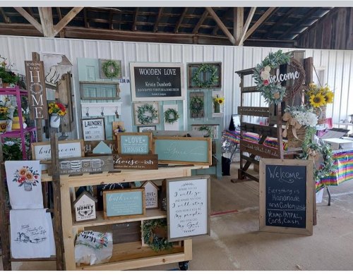 A display of handmade signs and decor in a rustic setting, featuring greenery and welcoming messages.