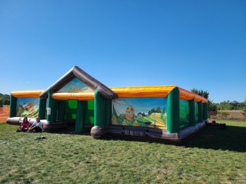 A colorful inflatable bounce house with a farm theme, set on a grassy field under a clear blue sky.