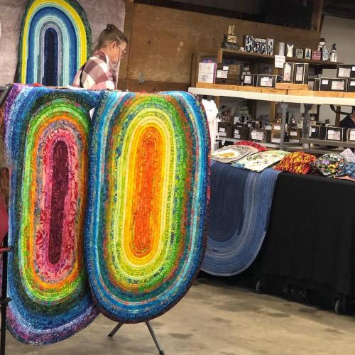 A colorful quilt display featuring vibrant circular patterns, with a person arranging items in the background.