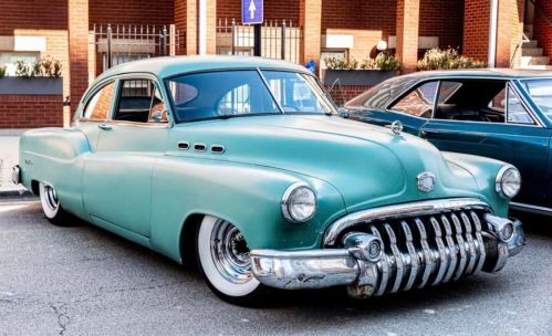 A vintage mint green car with a chrome grille parked on a city street, showcasing classic design and style.