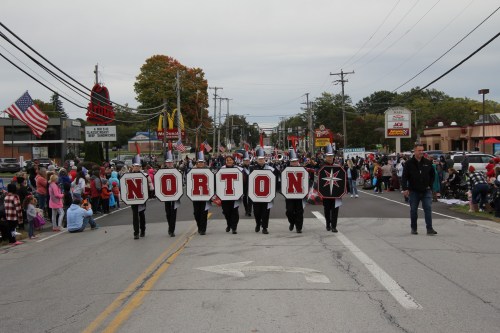 A parade with participants holding large letters spelling "NORTON," surrounded by spectators along the street.