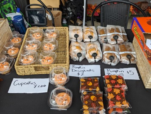 A table displays various baked goods, including cupcakes, pumpkin doughnuts, and pumpkin bars, with price tags.