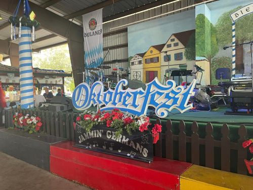 A festive stage setup for Oktoberfest, featuring a large sign and colorful decorations with flowers and musical notes.