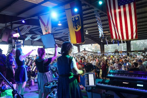 A lively festival scene with a band performing on stage, flags hanging above, and a large crowd enjoying the event.