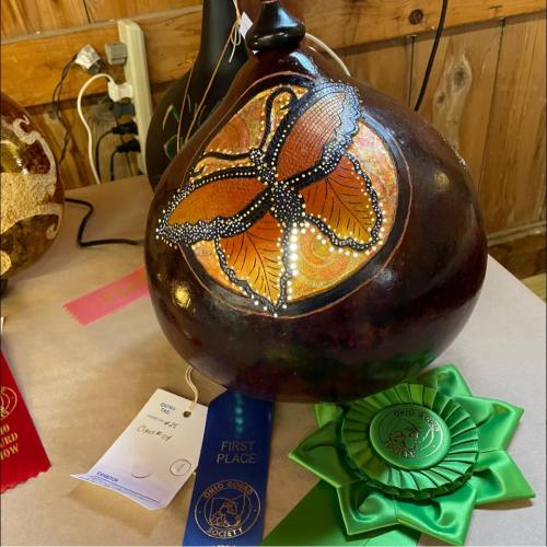 A decorative gourd featuring a butterfly design, displayed with first place and other award ribbons.