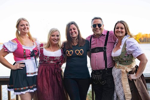 A group of five people in traditional attire posing together by a lake during a festive event.