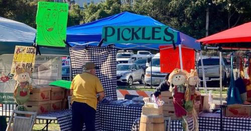 A market stall with a "Pickles" sign, featuring checkered tablecloths and colorful decorations, and a vendor organizing items.