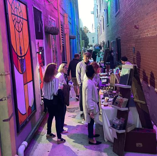 A vibrant alleyway with colorful murals, people browsing stalls, and a lively atmosphere during an outdoor event.