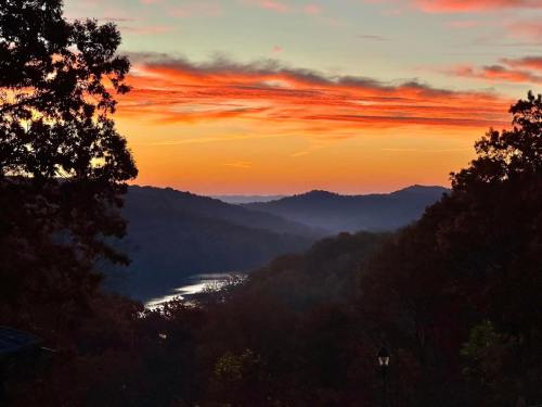 A vibrant sunset over rolling hills, with a river reflecting the colorful sky and silhouetted trees in the foreground.