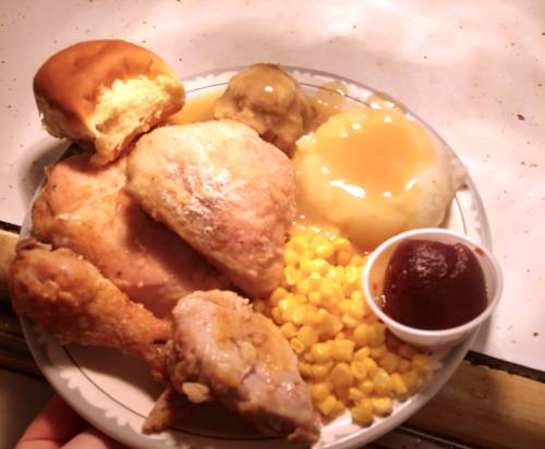 A plate of fried chicken, mashed potatoes with gravy, corn, a roll, and a small cup of jelly.