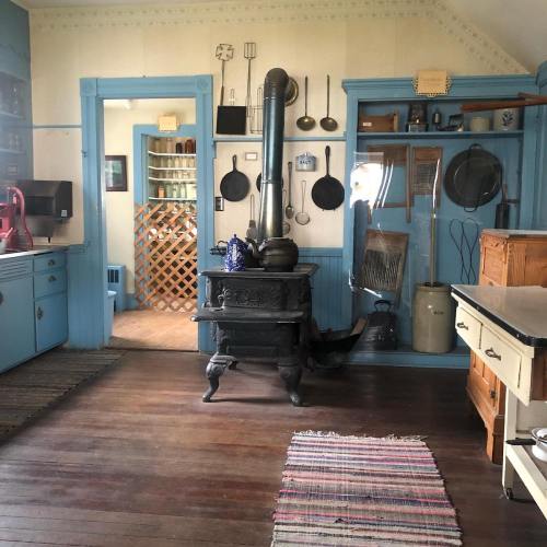 A vintage kitchen with blue cabinets, an old stove, wooden floors, and various kitchen utensils displayed on the walls.