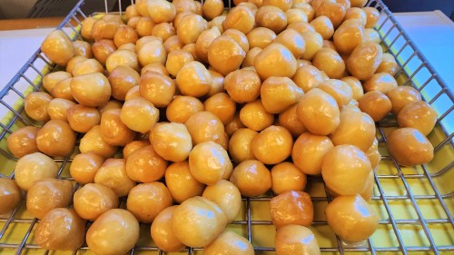 A close-up of a wire rack filled with shiny, golden-brown doughnut holes.