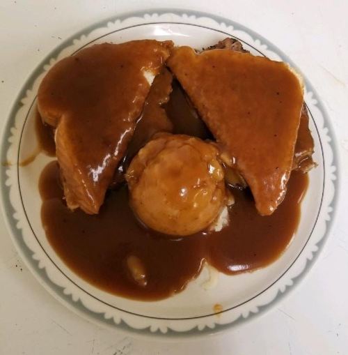 A plate with two slices of bread and a scoop of mashed potatoes, all covered in brown gravy.
