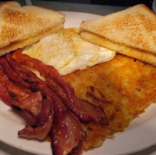 A plate of breakfast featuring crispy bacon, a fried egg, hash browns, and two slices of toasted bread.