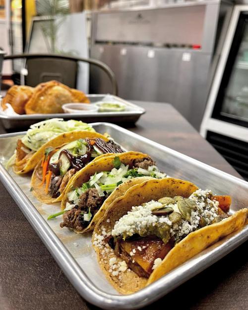 A platter of colorful tacos with various fillings, garnished with onions and cilantro, served in a casual dining setting.