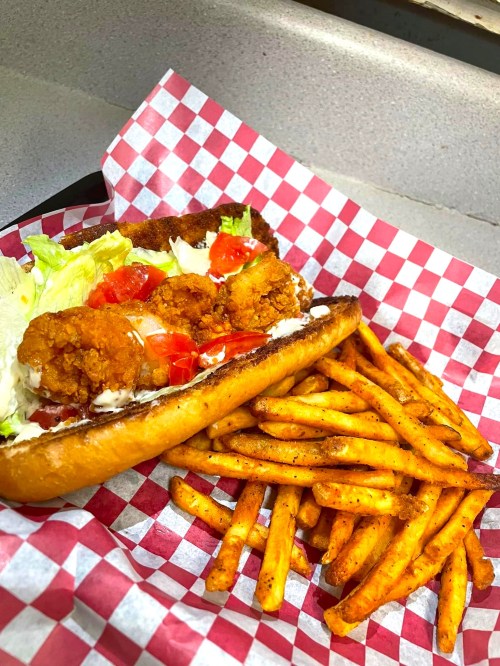 A crispy chicken sandwich with lettuce and tomatoes, served with a side of seasoned fries on a checkered paper tray.