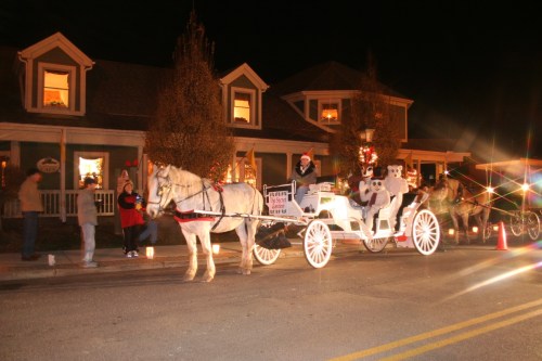 A horse-drawn carriage decorated for the holidays, with people in festive attire and a cozy house in the background.