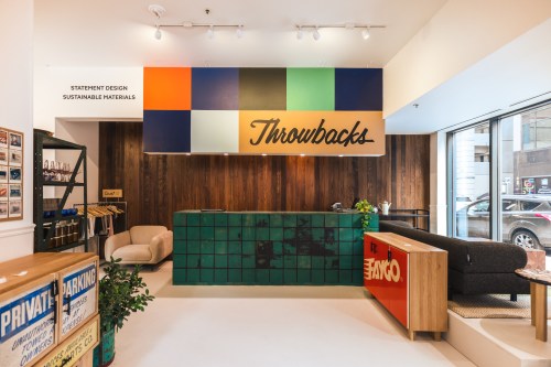 Interior of a modern reception area with a colorful "Throwbacks" sign, green tiled counter, and stylish furniture.