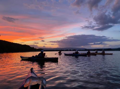 A group of kayakers paddles on a calm lake at sunset, with vibrant colors reflecting on the water.