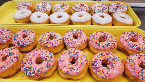 A tray of colorful donuts: pink frosted with sprinkles and white frosted, arranged neatly on a yellow tray.
